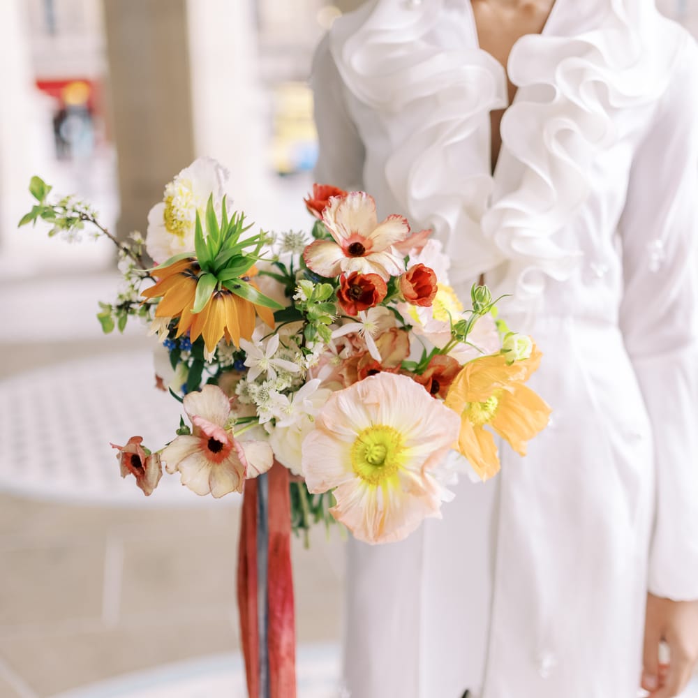 Bride wears ruffled wedding gown with split front and holds floral pastel bouquet 