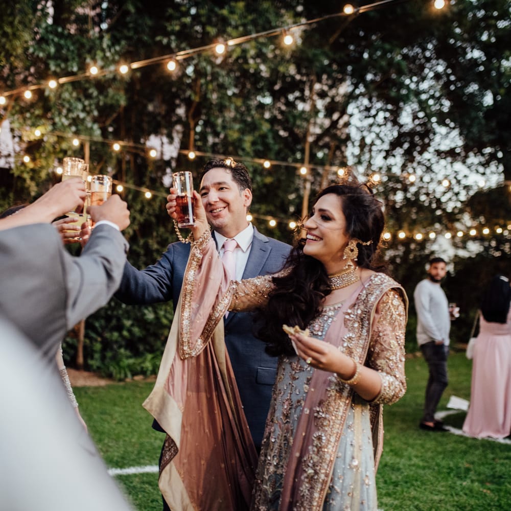 Bride lifts glass in celebration with groom as twinkling lights hang above