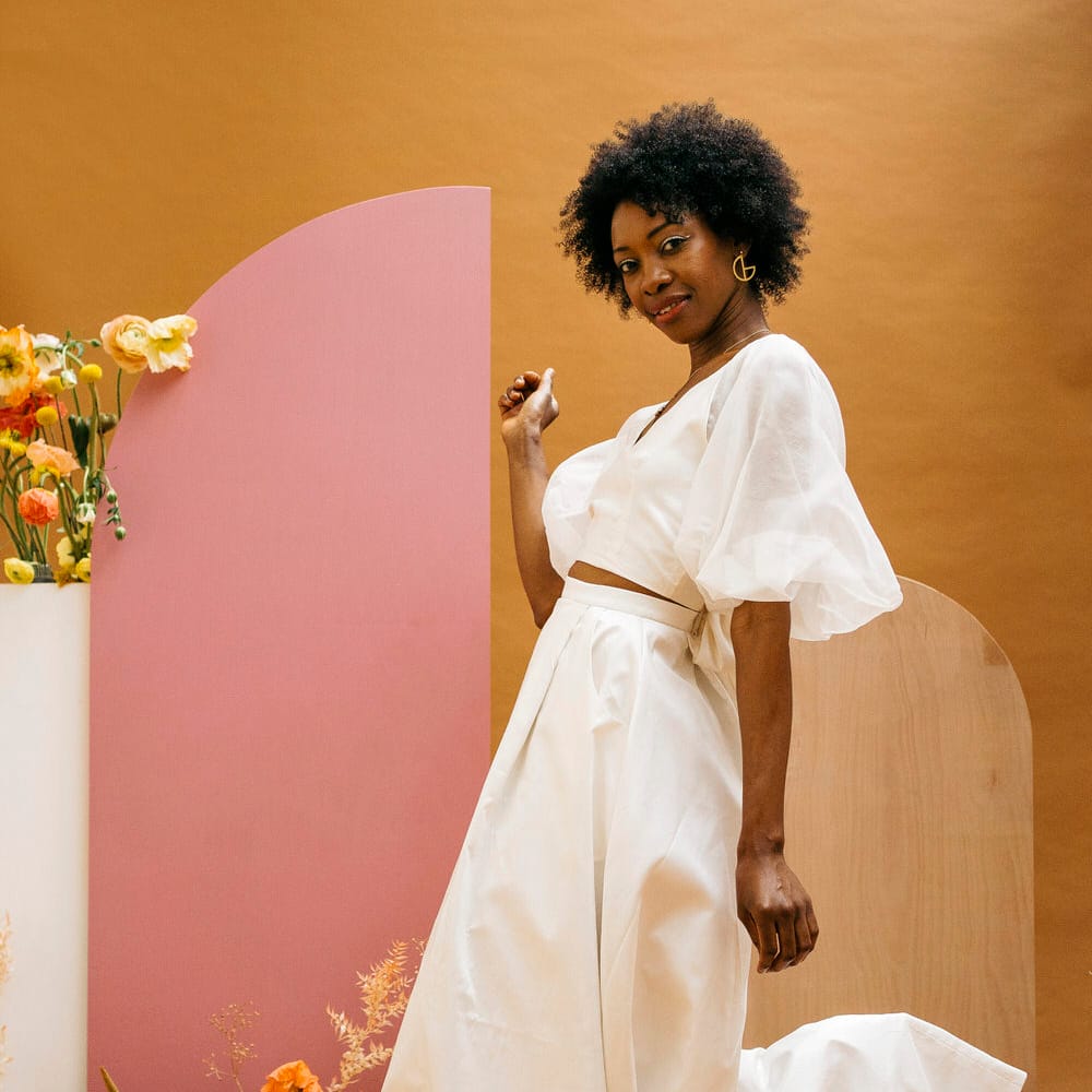Bride rocking sleek wedding separates next to a mustard and pink background with pink, yellow and neutral florals