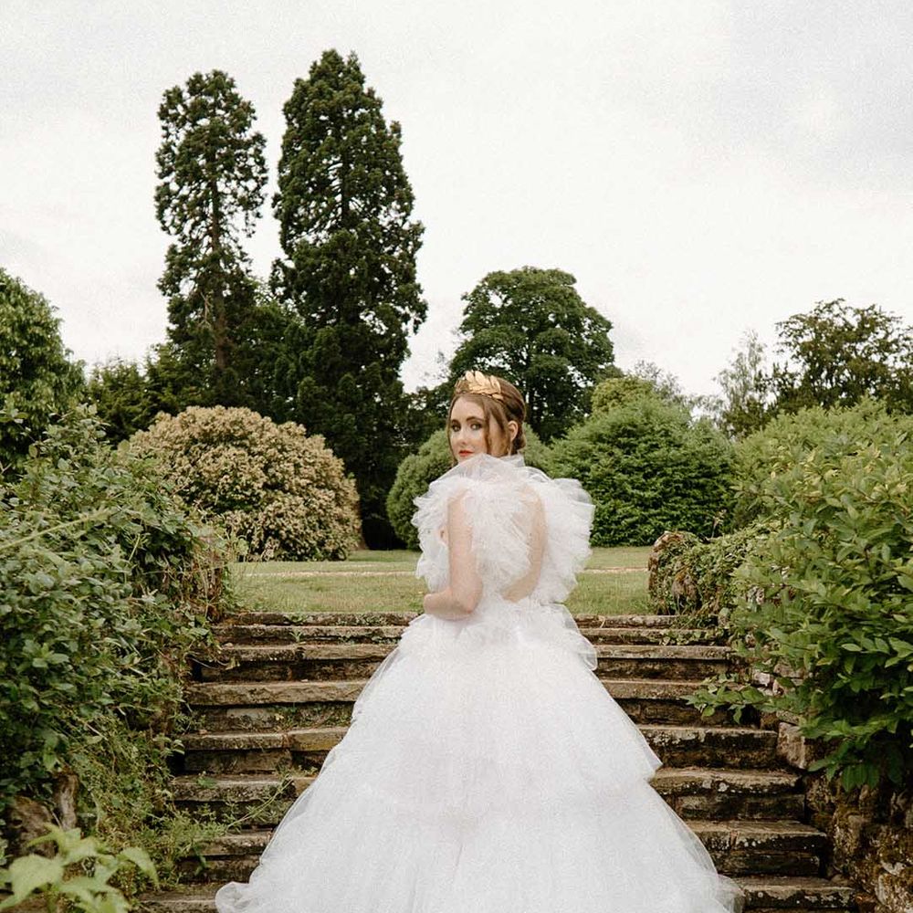 Bride in a tulle wedding dress standing on the steps in the gardens at Bourton Hall wedding venue 