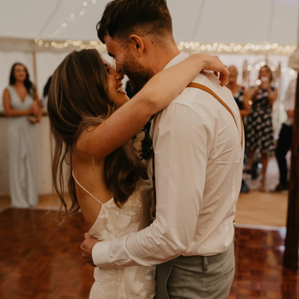 Bride wraps her arms around groom as they dance during marquee reception | Mark Bamforth Photography
