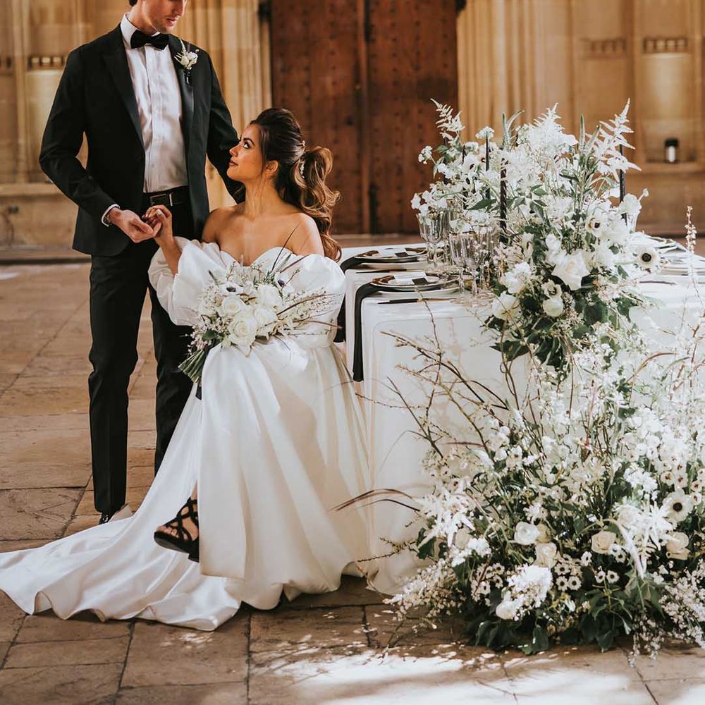 Bride in a Nortier Shallow wedding dress sitting at the intimate reception decorated with white flowers at Bodleian Library 