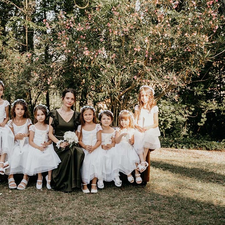 Bridesmaid wearing deep green silk dress sits beside flower girls who wear white floral crowns | Royal Studio