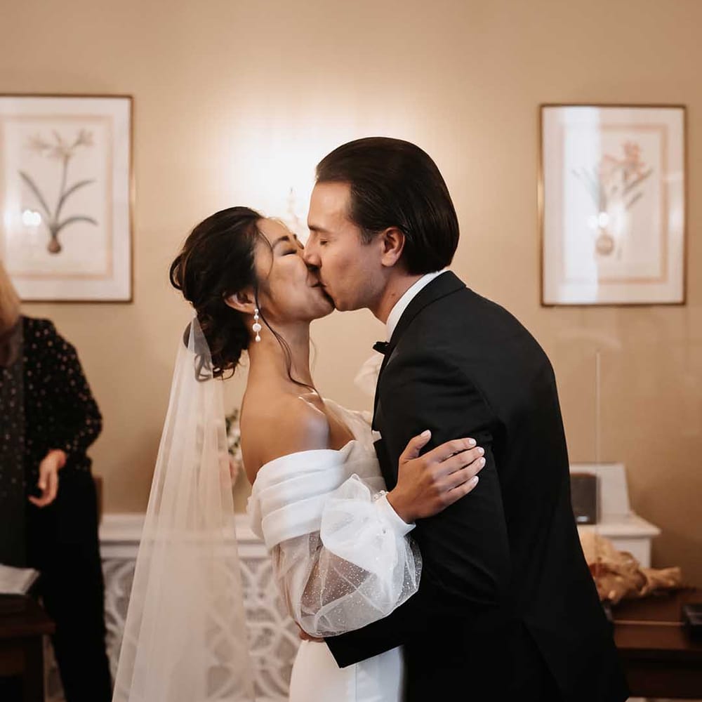 Bride in sophisticated wedding dress and Groom in Black suit kissing in Town Hall wedding