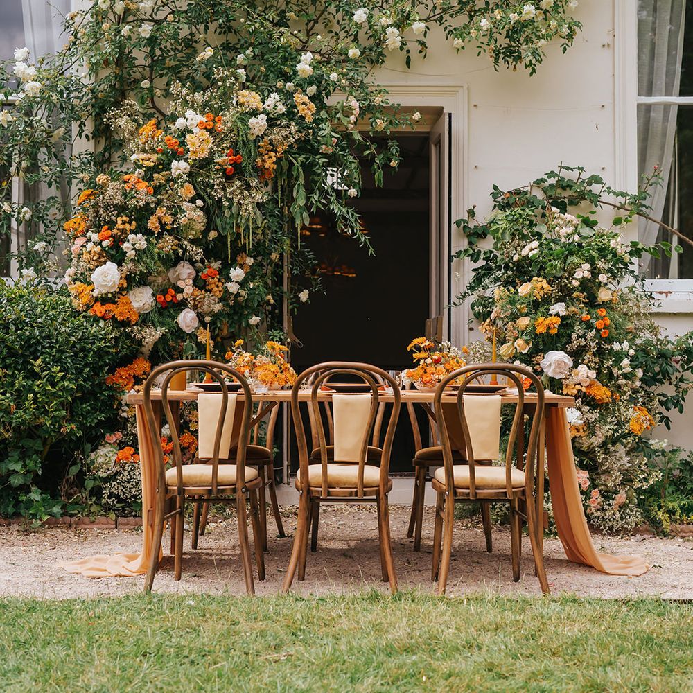Orange outdoor wedding tablescape with floral arrangement, wooden furniture and table decor 