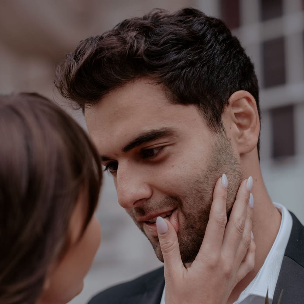 Bride with white almond shaped wedding nails touching her grooms face