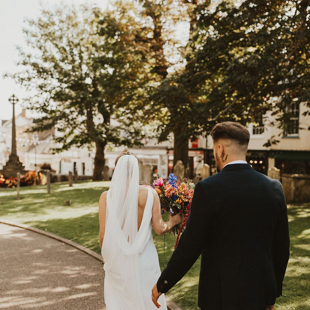 Groom in a navy suit following his bride in a cowl back slip wedding dress and cathedral length veil 