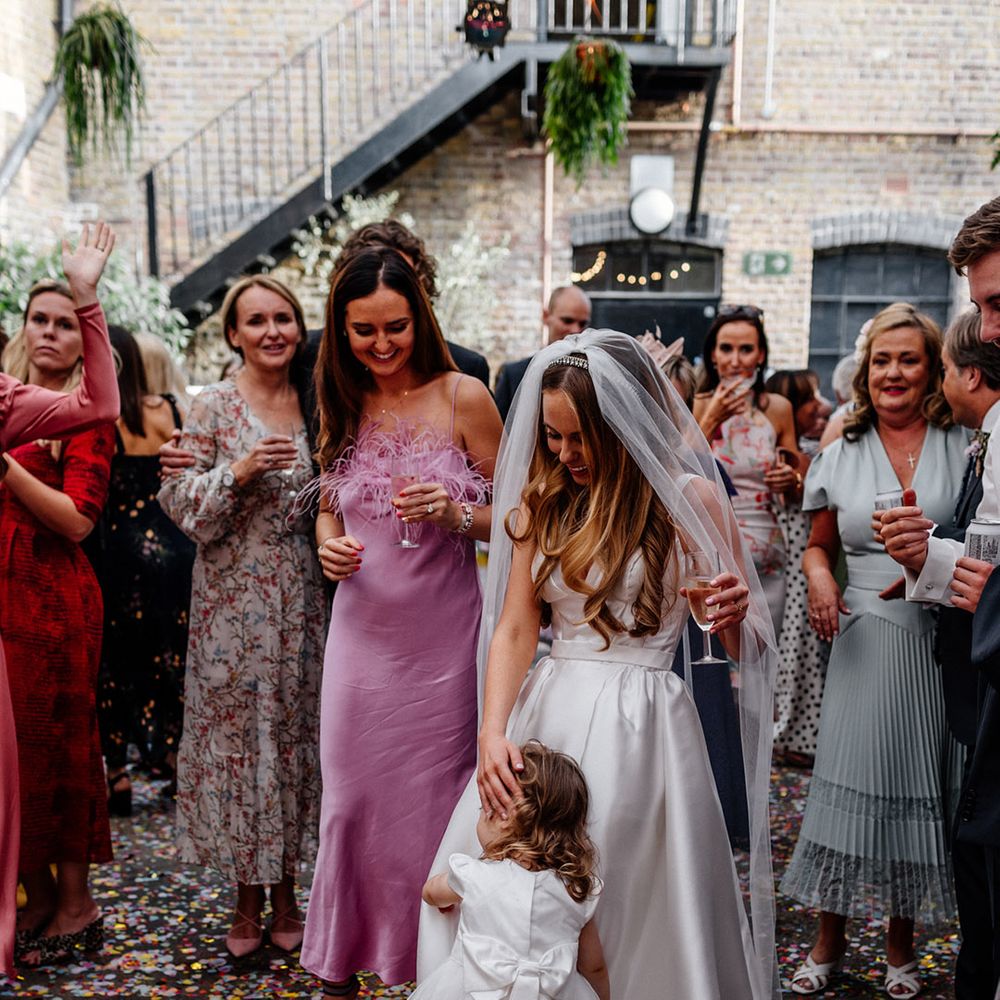 Flower girl in a white dress with tulle skirt hugging the bride in a princess wedding dress and veil 