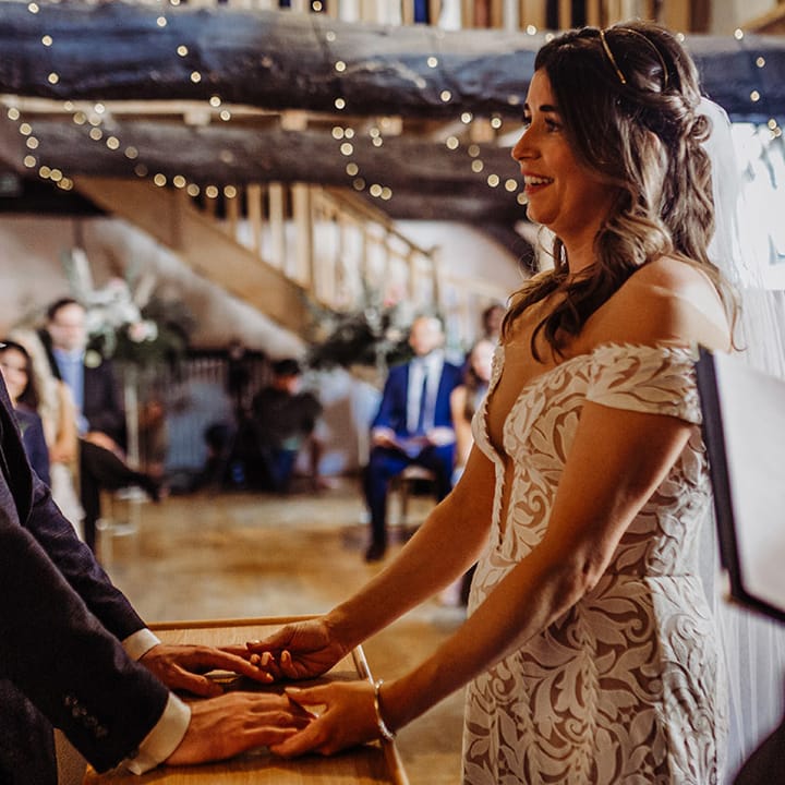 Bride looks adoringly at the groom in a blue suit as they hold hands for their wedding ceremony 