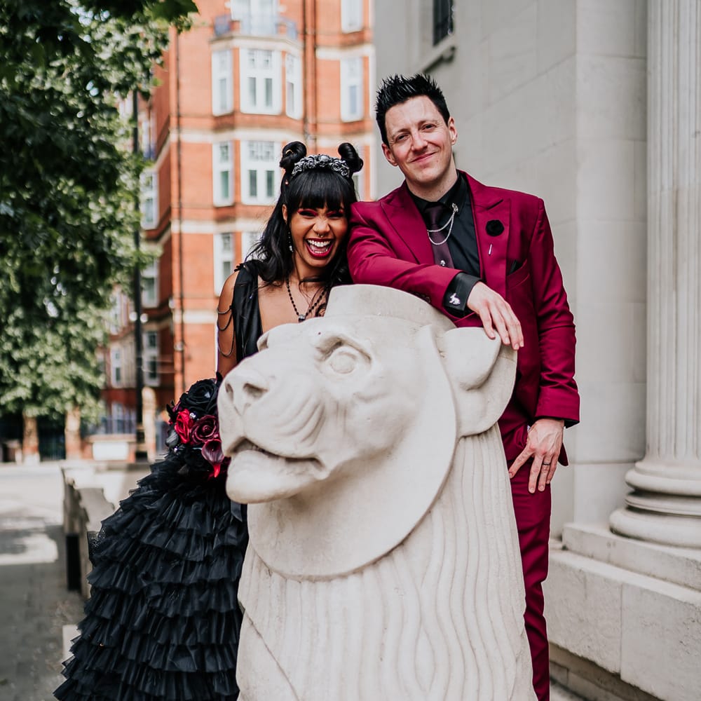 Bride & groom sit on stone lion for couples portraits on their wedding day