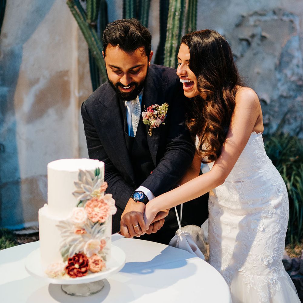 Bride & groom cut two tier wedding cake with white frosting and colourful frosted florals 