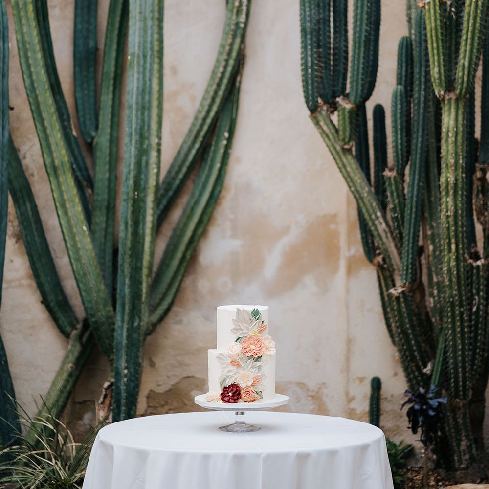 Two tier white frosted wedding cake complete with brightly frosted floral decor to one side
