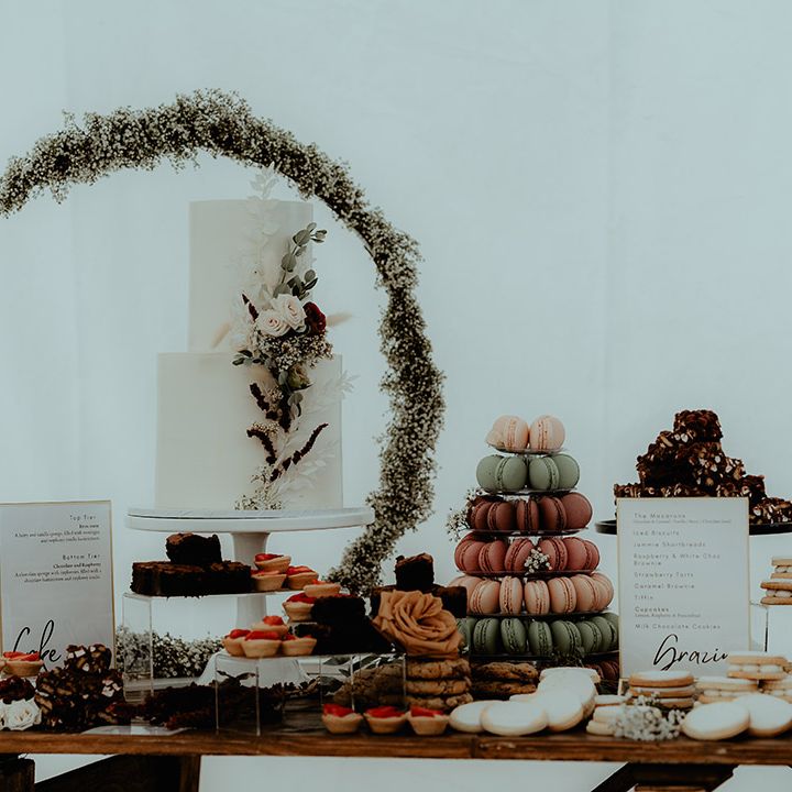 Dessert table with macarons, cupcakes, biscuits and the two tier white iced wedding cake with a half moongate 
