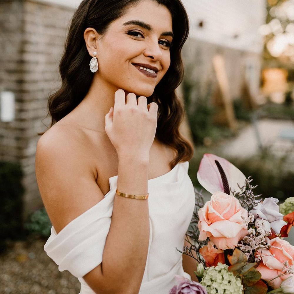 Bride with dark lipstick and gold eyeshadow in an off the shoulder wedding dress holding a pretty wedding bouquet 