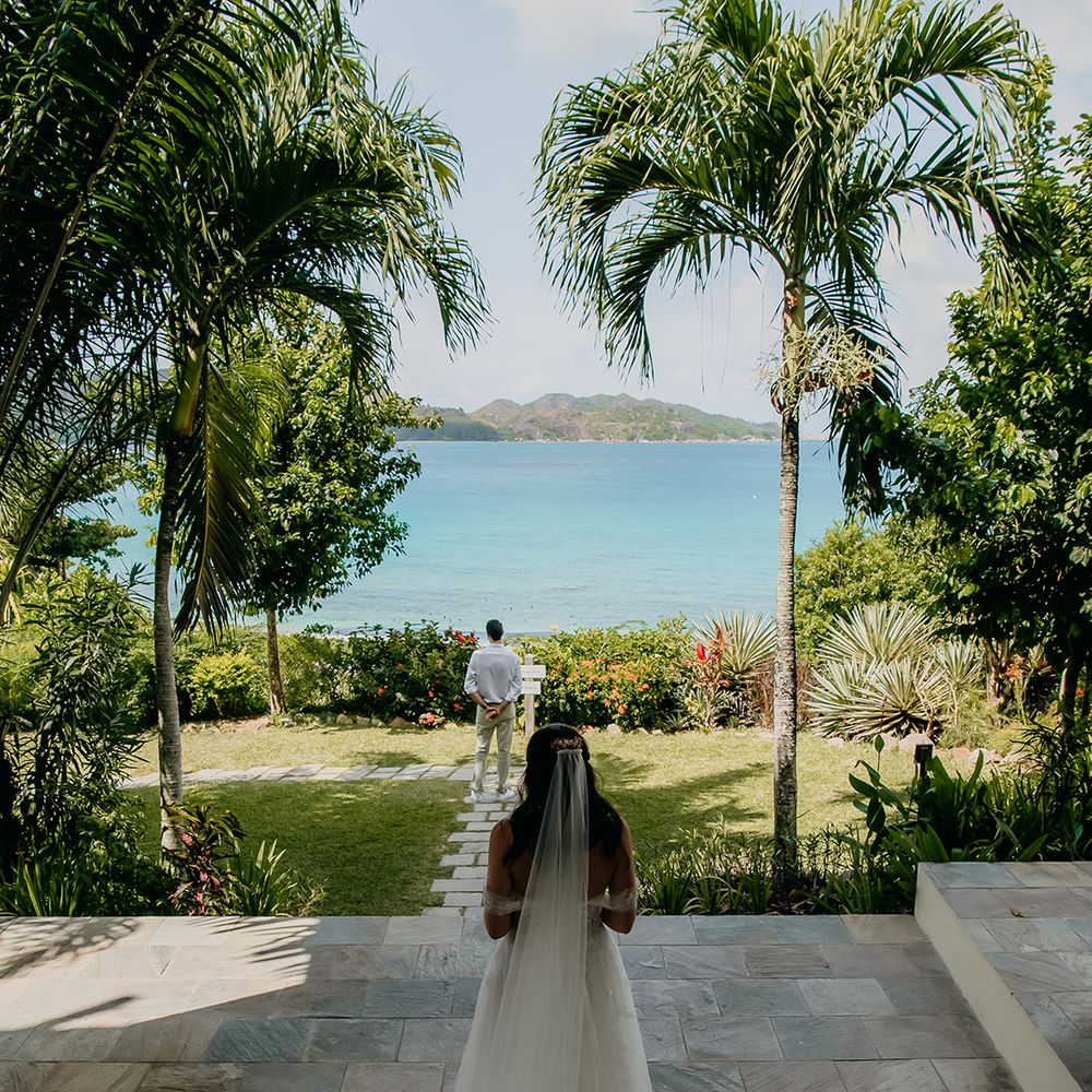 Bride in off the shoulder lace wedding dress with sweetheart neckline and lace floral details and cathedral length veil walking to groom at Seychelles elopement