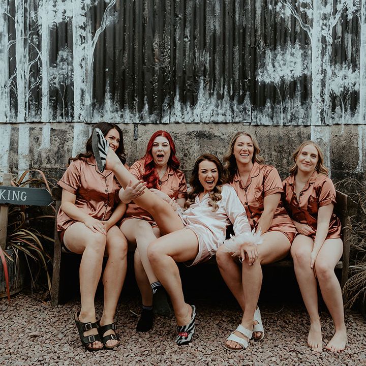 Bridesmaids in burnt orange satin pyjamas with the bride in pink satin pyjamas with pink feather cuffs 