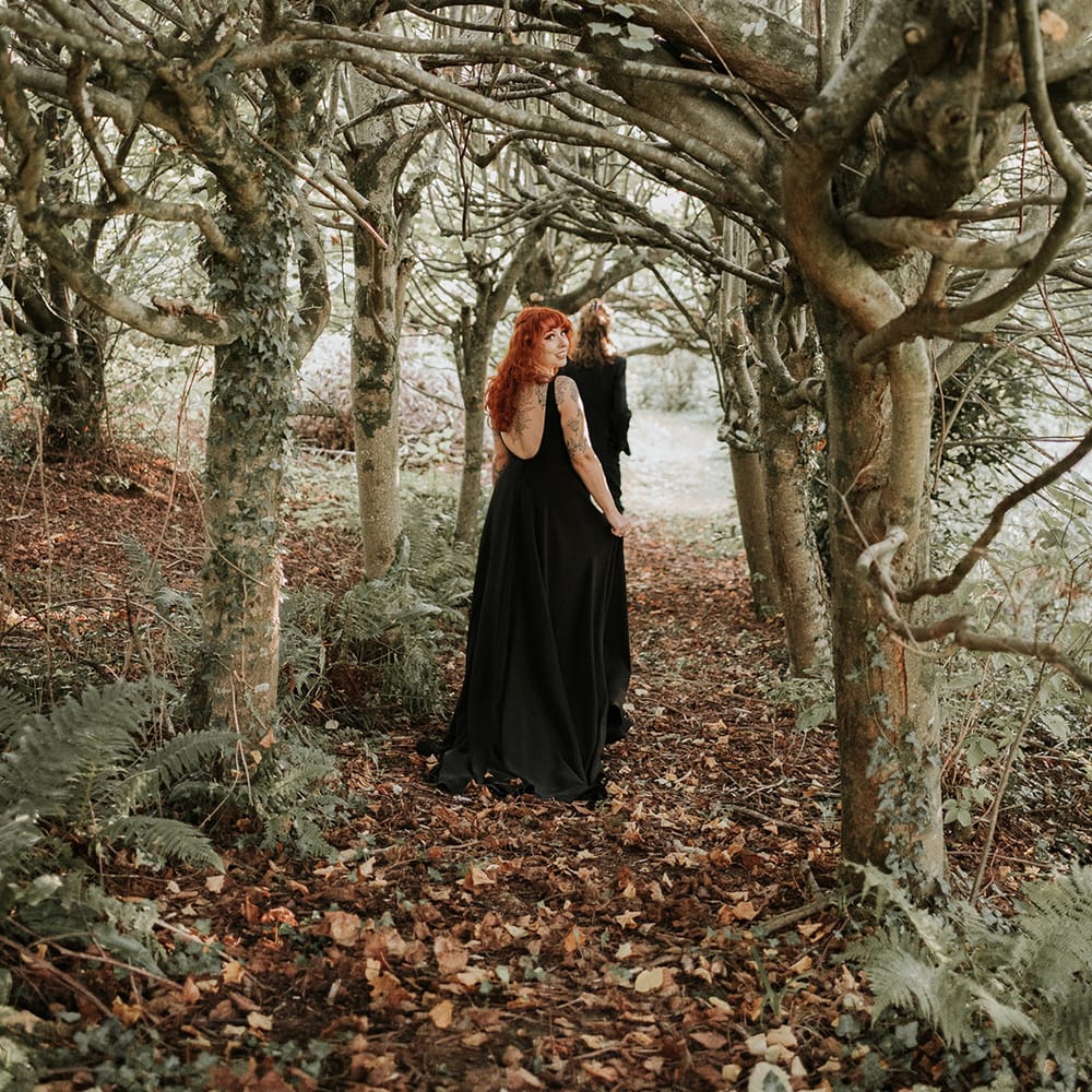 Bride in open back detail black wedding dress walking through the woods at Westcott Barton Devon wedding venue 