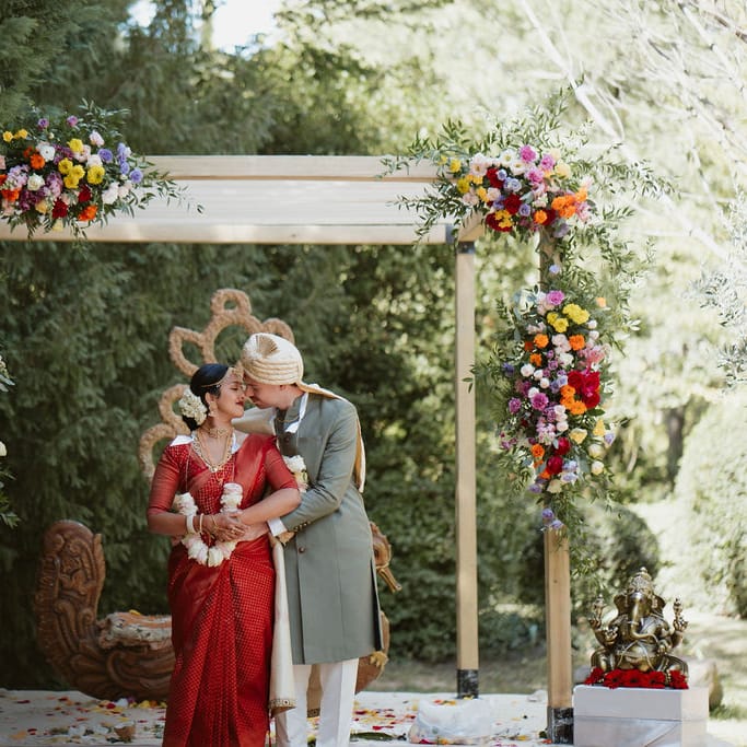 Bride in a red lehenga and groom in a green Sherwani kissing at their Hindu wedding in Provence 