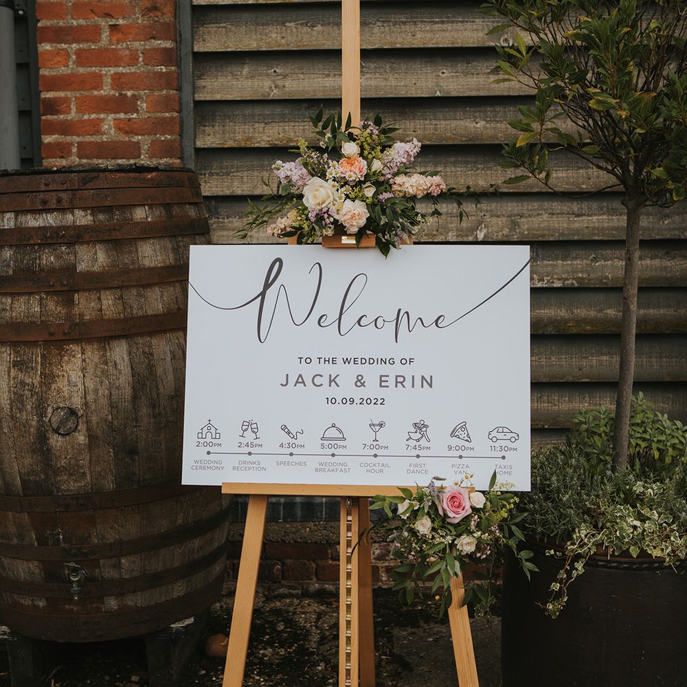 Black and white wedding welcome and order of the day sign on a wooden easel with pastel flowers for Dove Barn Weddings 