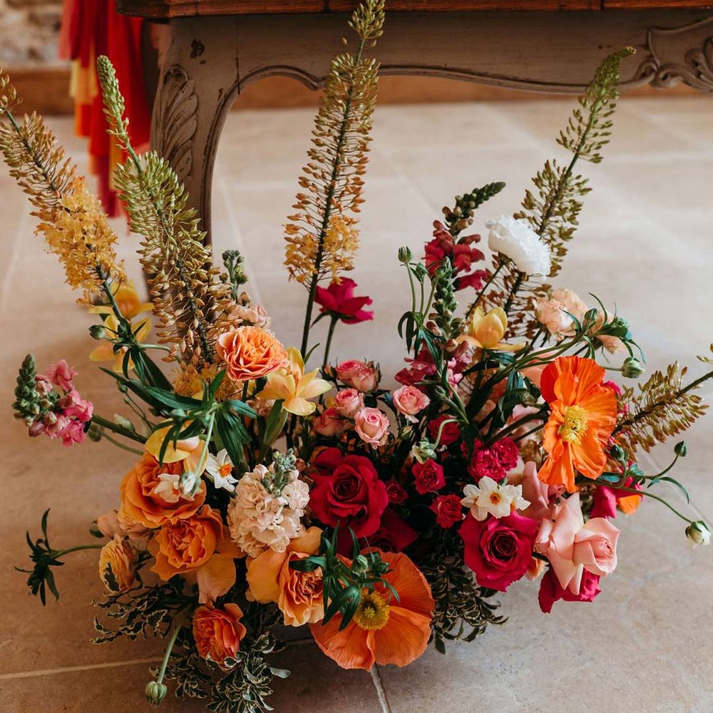 Seasonal wedding flower arrangement with pink and orange garden roses, orange floribunda, yellow ranunculus flowers, foliage and Iceland poppies 