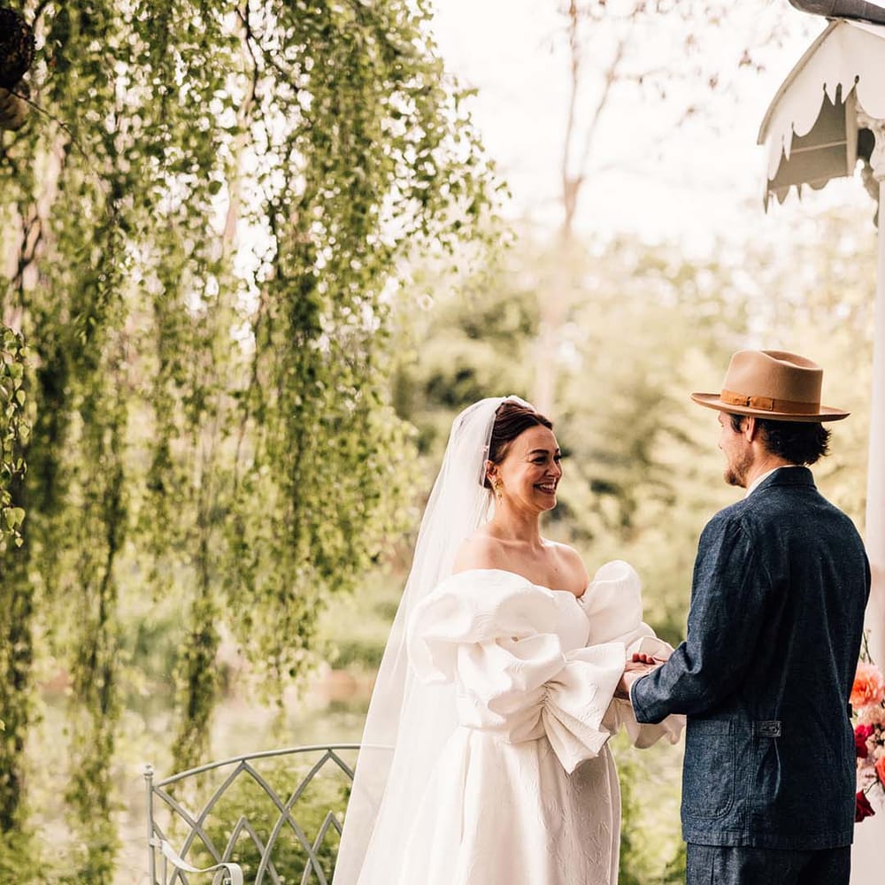 An outdoor wedding at Preston Court in Kent with the bride and groom holding hands at the altar 