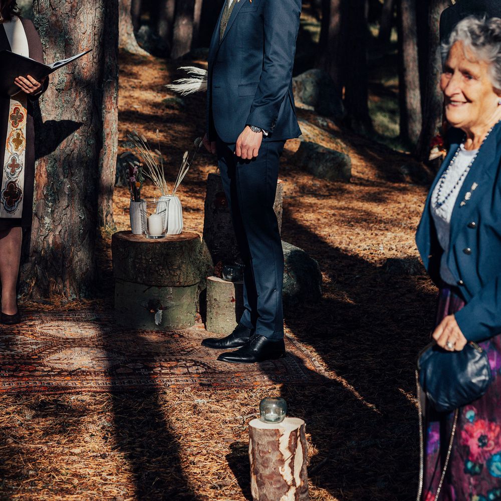 Grooms awaits bride during outdoor ceremony with strung lights in the background
