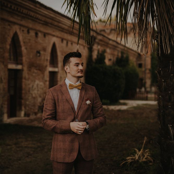 Stylish groom in a brown wedding suit with check pattern and ochre bow tie for autumn wedding 