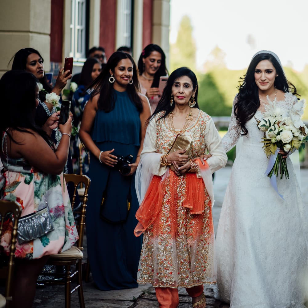 Bride walks down the aisle with her mother who wears a bright and colourful saree