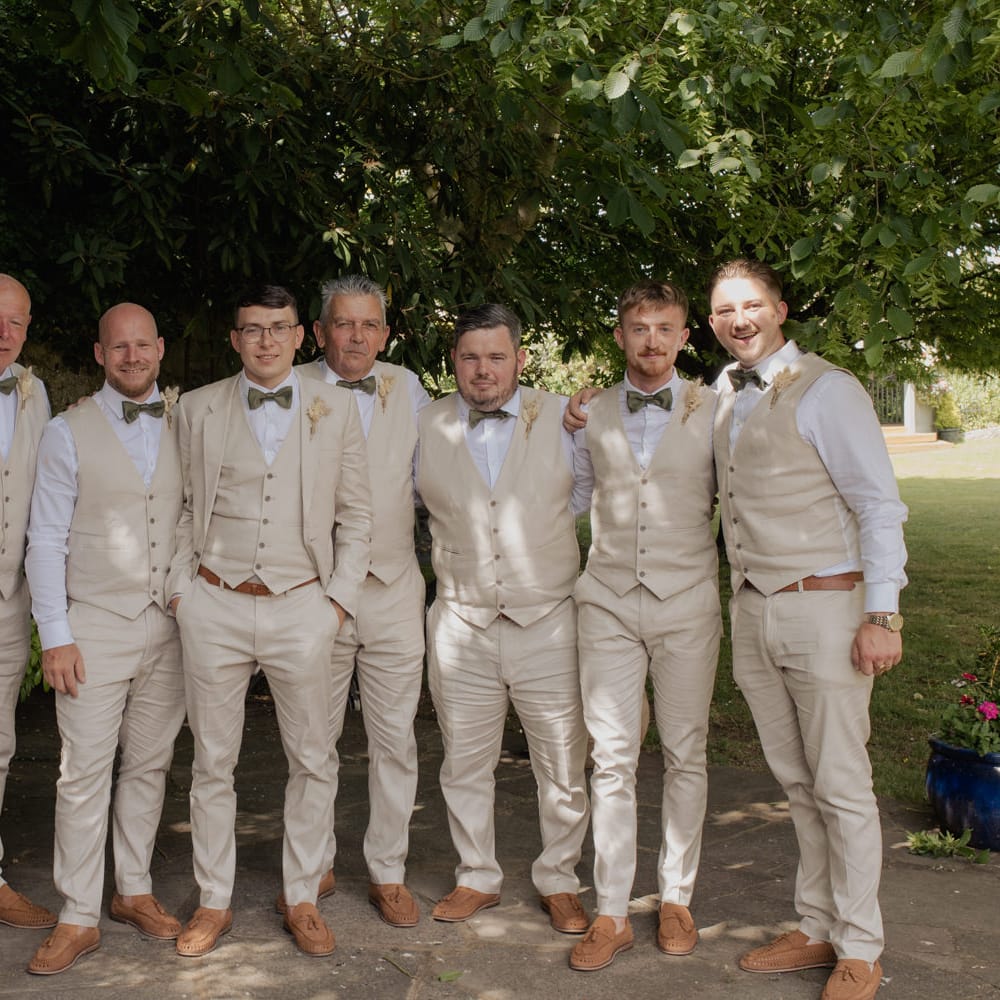 Groom and groomsmen in beige suits, waistcoats and sage green bow ties 