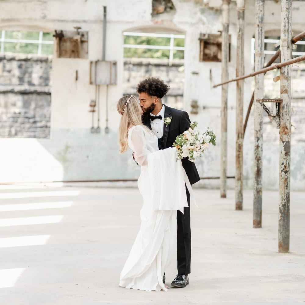Groom with afro hair kissing his bride with sleek straight hair wearing a halo headdress 