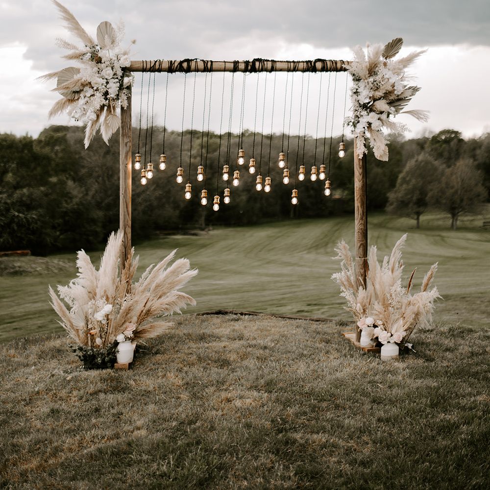 Wooden frame decorate with hanging Edison bulbs and dried palm leaves and pampas grass floral arrangements 