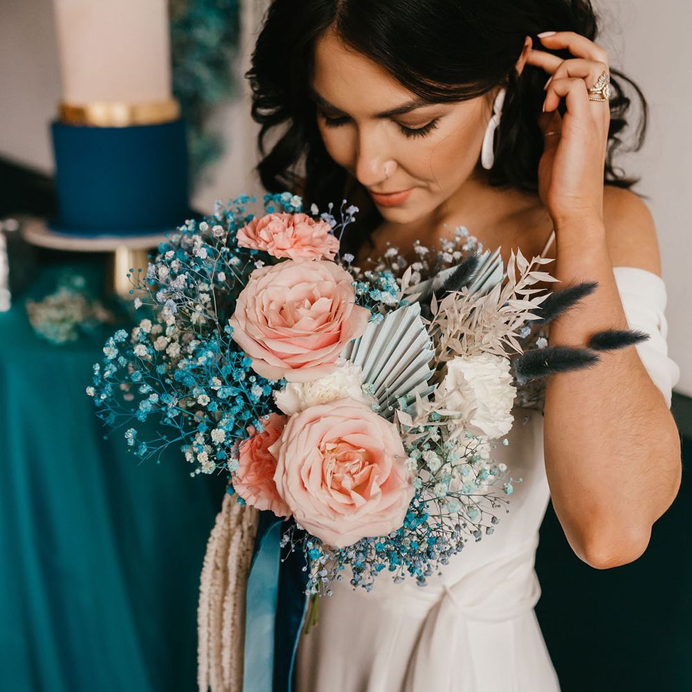 Bride with wishbone rings on tucking her wavy hair behind her ear holding her pink rose and teal gypsophila wedding bouquet 