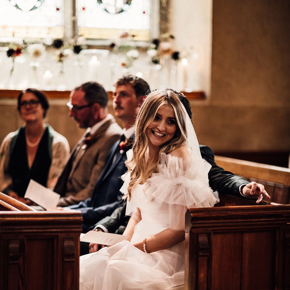 Bride in white Halfpenny London Mayfair dress sits in pew during church wedding ceremony in Cornwall