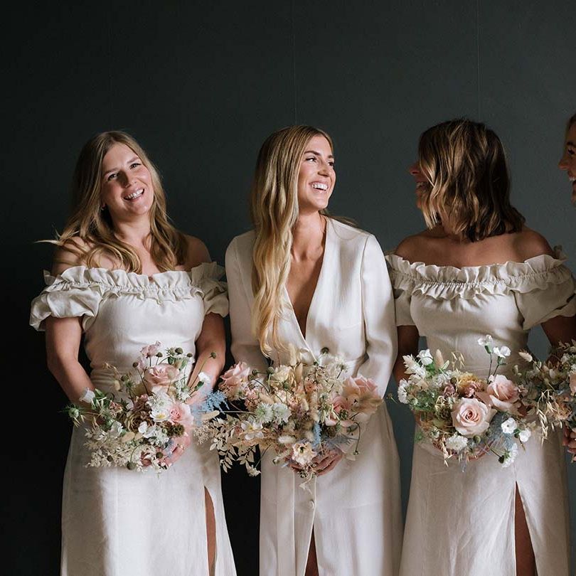 Bride with long blonde hair with bridesmaids in off the shoulder off white dresses with pastel summer bouquets