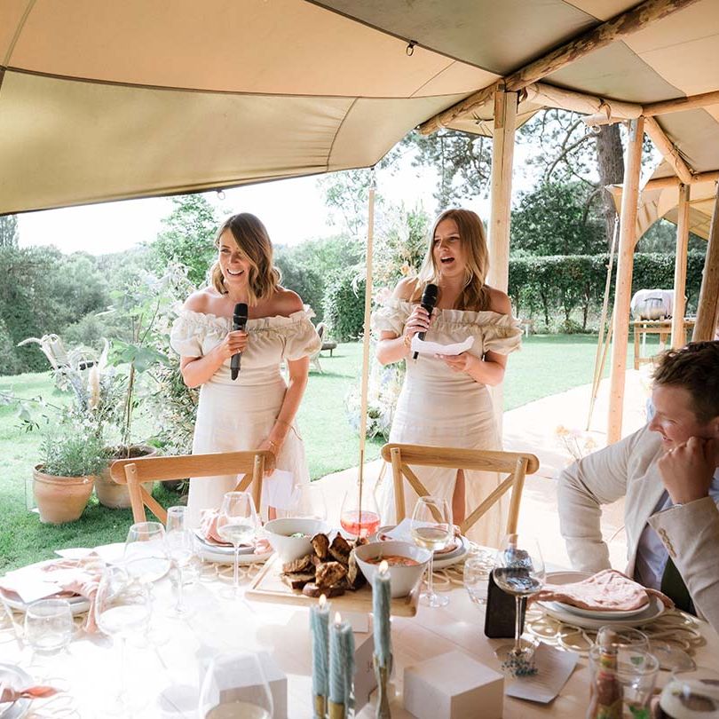 Bridesmaids in off the shoulder white dresses give their wedding speeches at circular tables inside the Buffalo Tipi