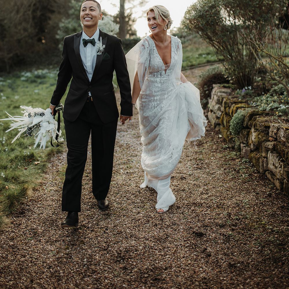 LGBTQI+ couple holding hands at Hodsock Priory wedding in black tie suit and lace wedding dress