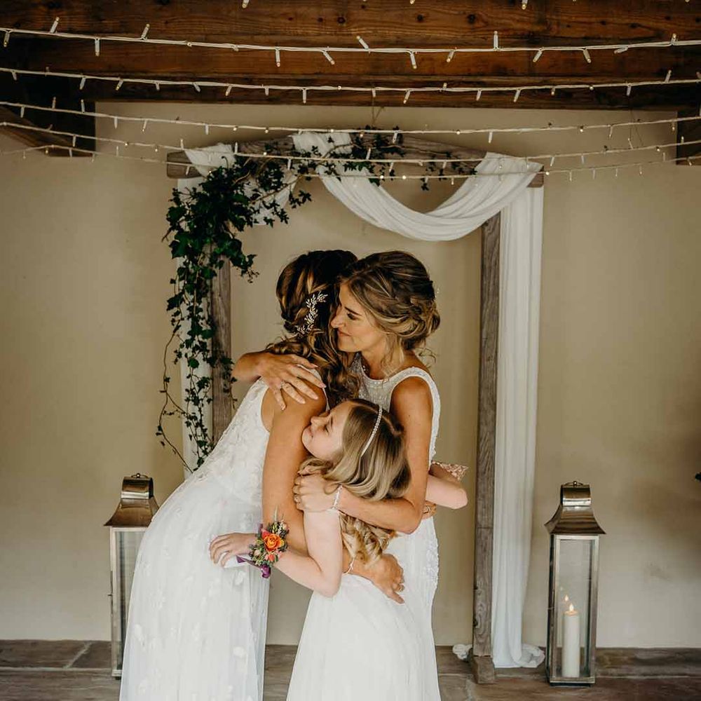 Same sex wedding ceremony at Ever After Wedding Venue with brides embracing their daughter during the nuptials 