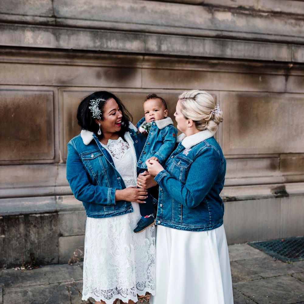 Lesbian wedding with two brides holding their son in matching denim jackets 