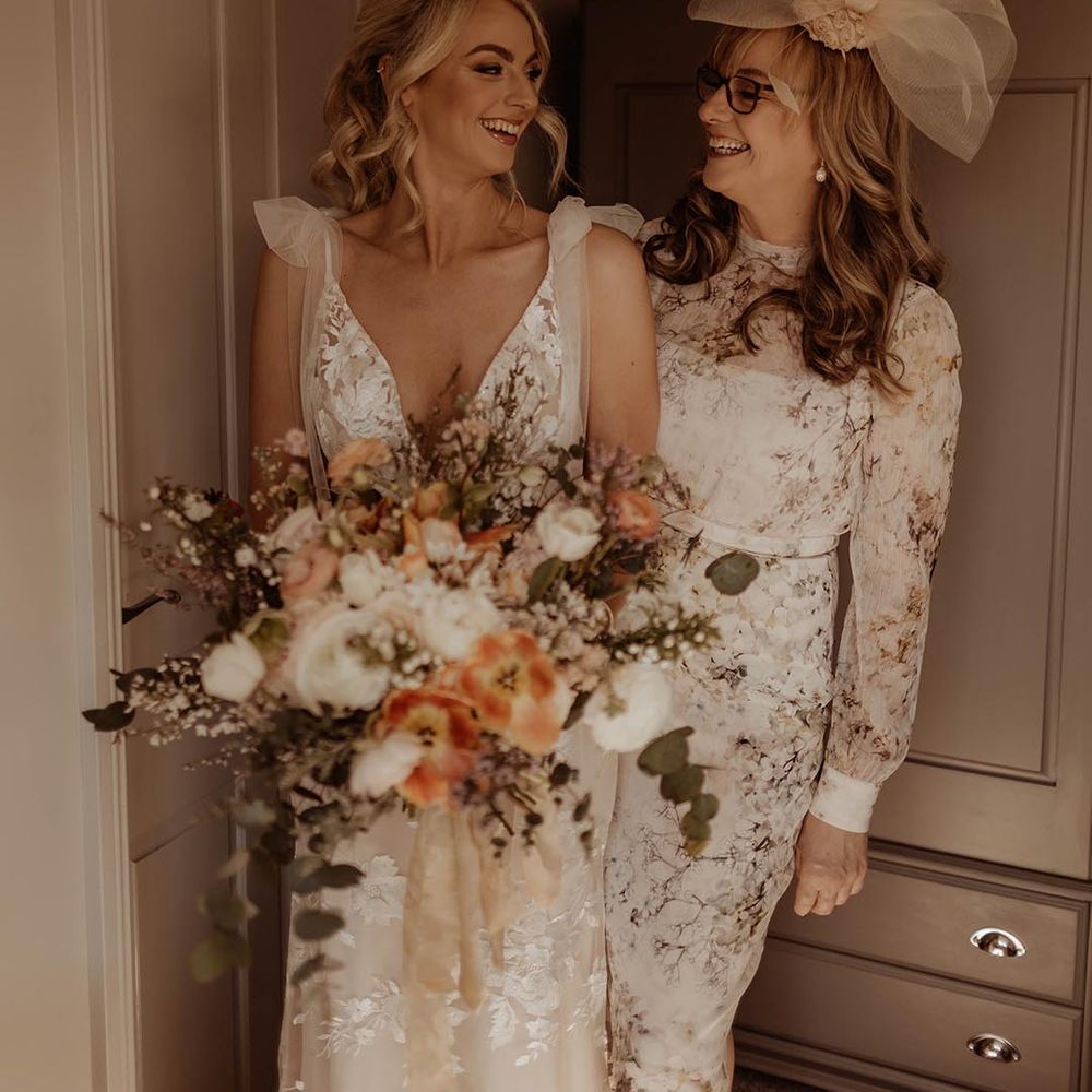 Bride carrying autumnal wedding bouquet with her mother wearing a fascinator and floral pattern dress 