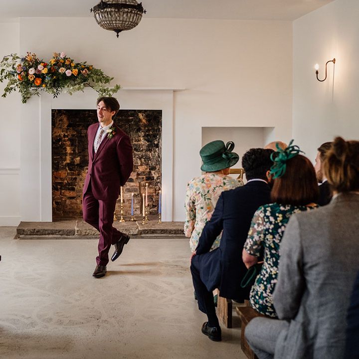 Groom in three piece burgundy suit waits nervously at the altar for the bride on their wedding day at Aswarby Rectory