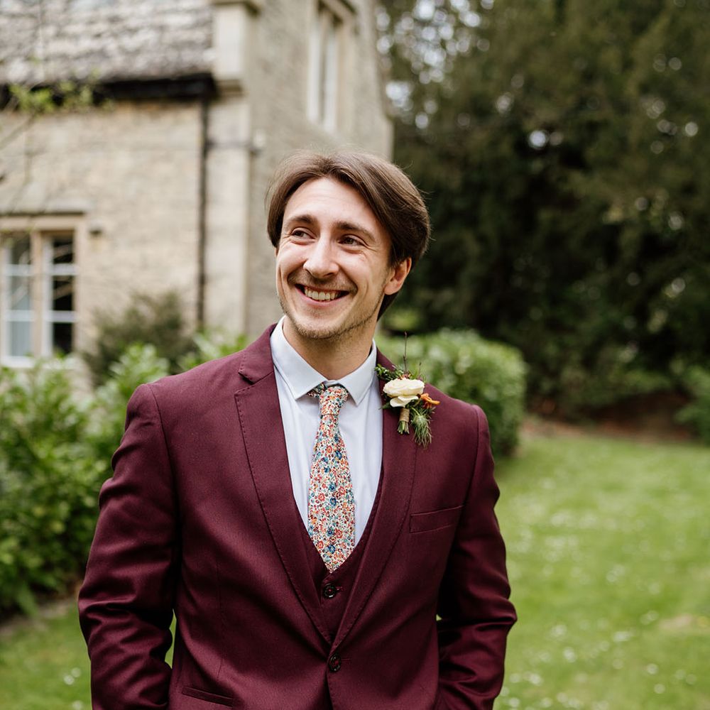 Groom in three piece burgundy suit with patterned tie and white shirt 