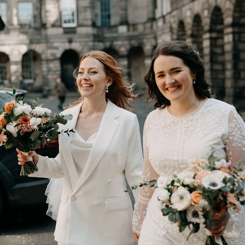 Brides walk alongside one another in bridal suit and boho wedding gown