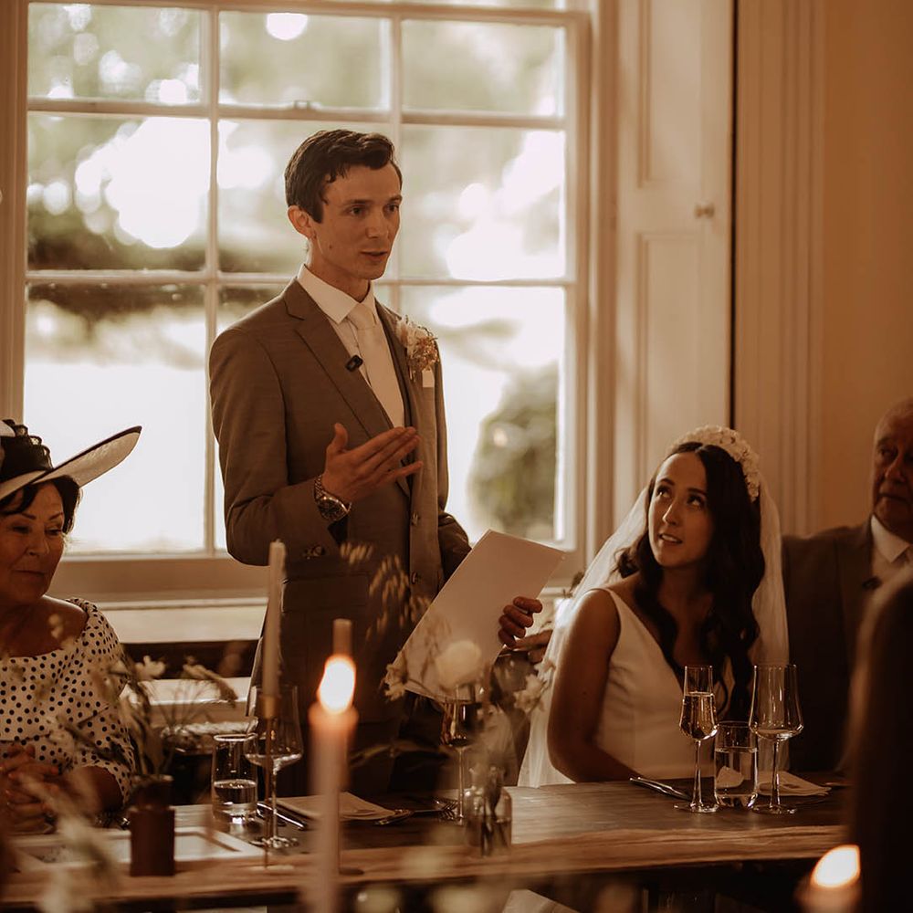 Bride looks up at the groom as he reads out his wedding speech for their neutral boho luxe wedding at Aswarby Rectory 