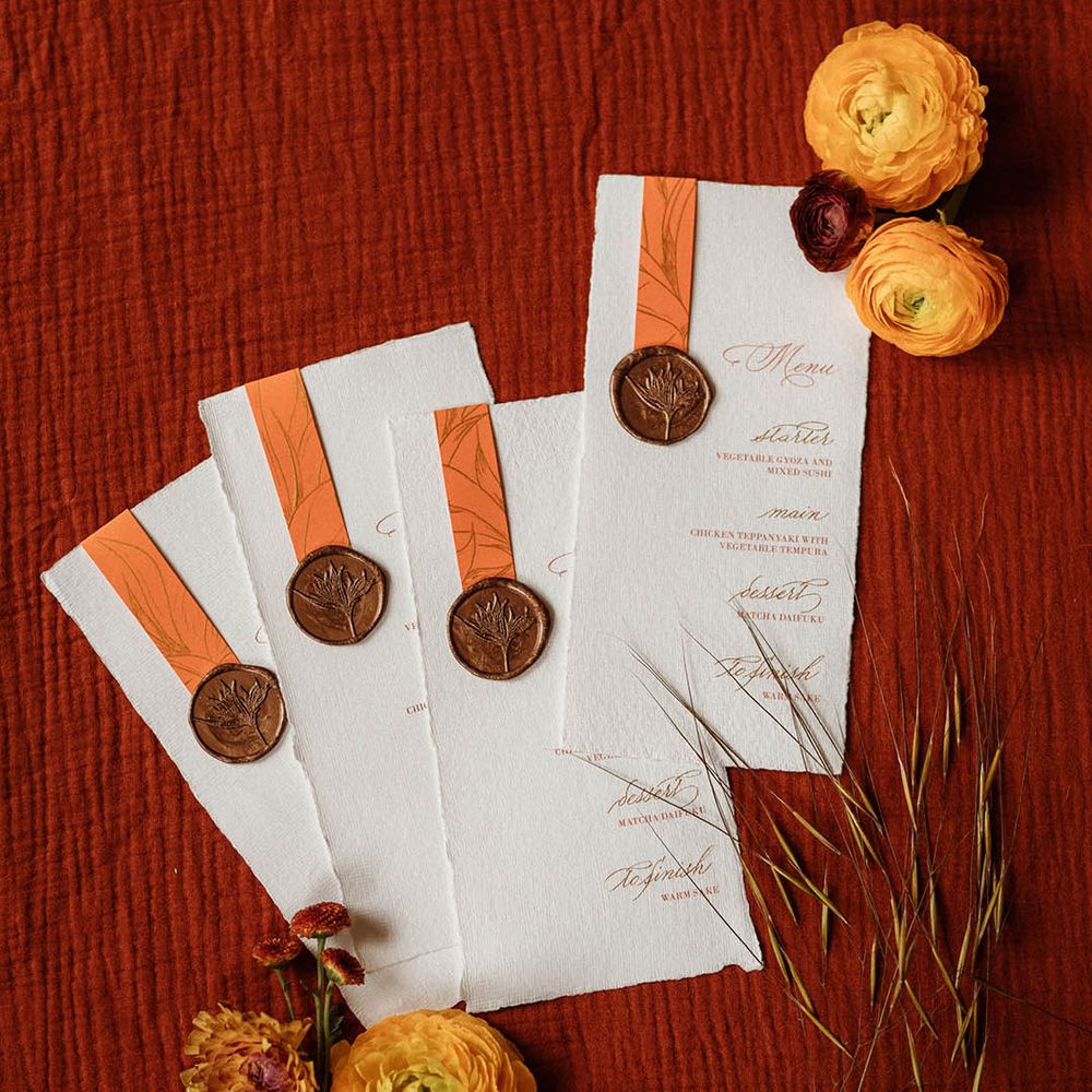 Menu cards written in gold calligraphy with orange design held on by a copper wax seal 