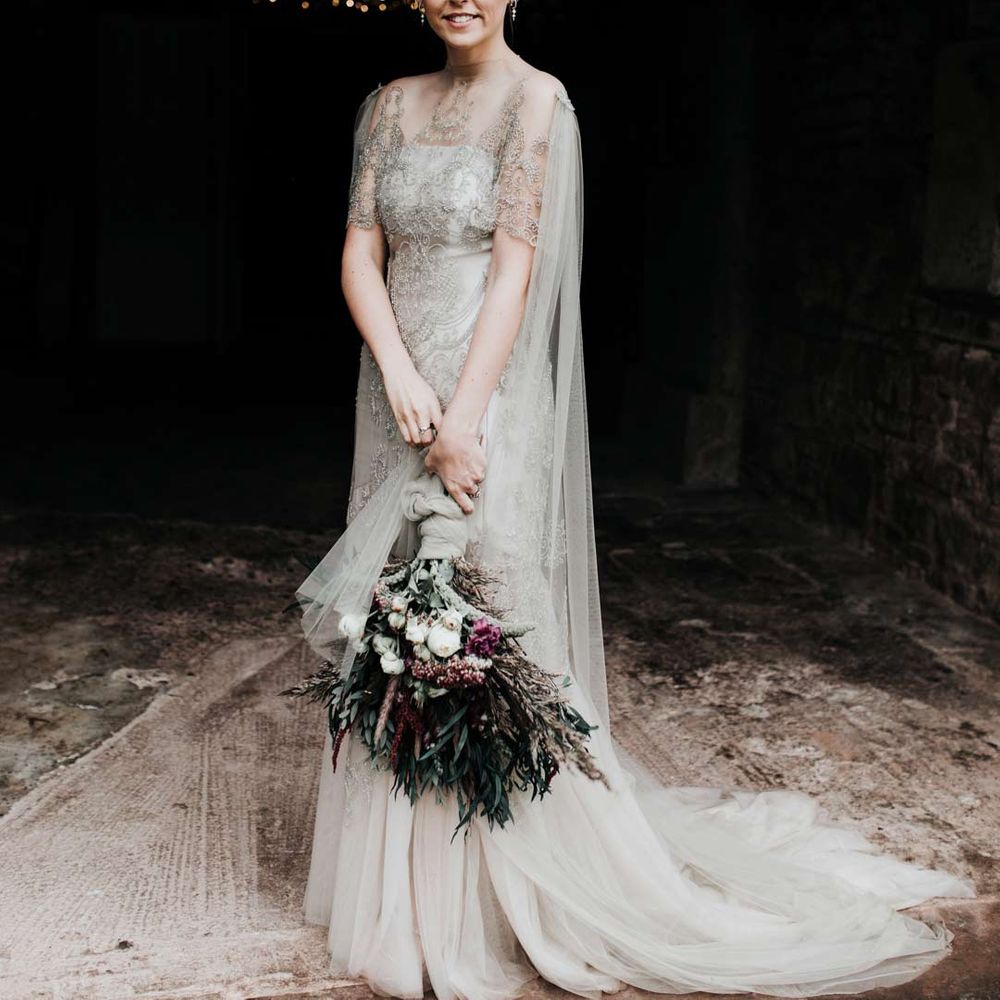 Bride in homemade sage tinted quarter length sleeve wedding dress with homemade bouquet with peacock feather detailing