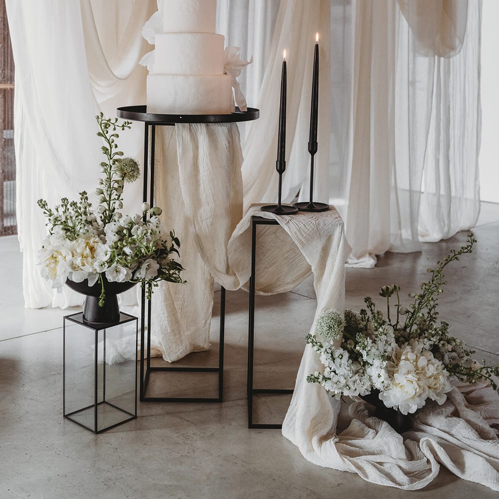 Large vegan three tier wedding cake with black taper candles and other decor with white wedding drapes and flowers 