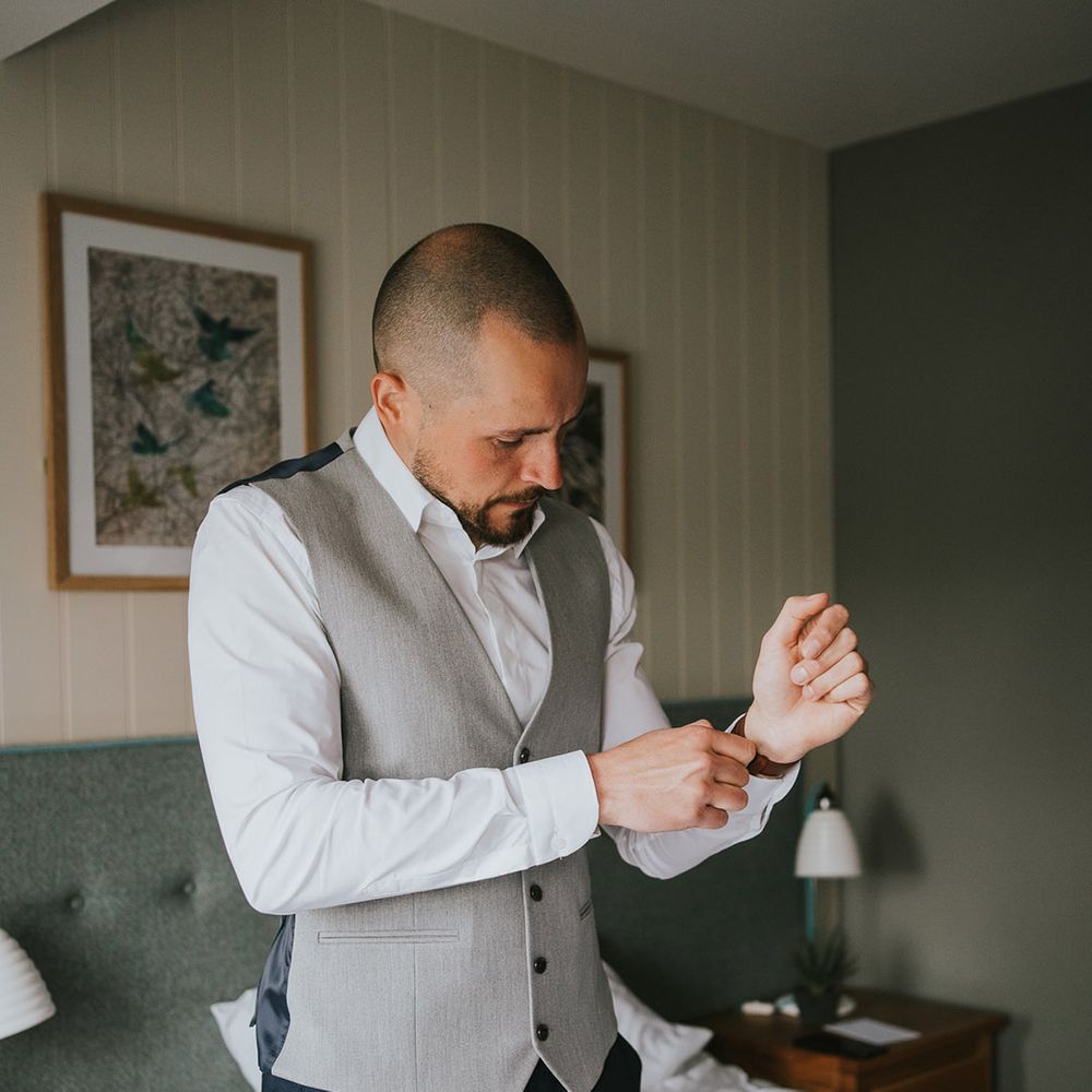 Groom in a grey waistcoat doing putting on a brown leather strap watch