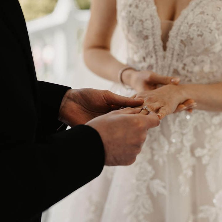 Groom in a black three piece suit puts on the bride's wedding ring 