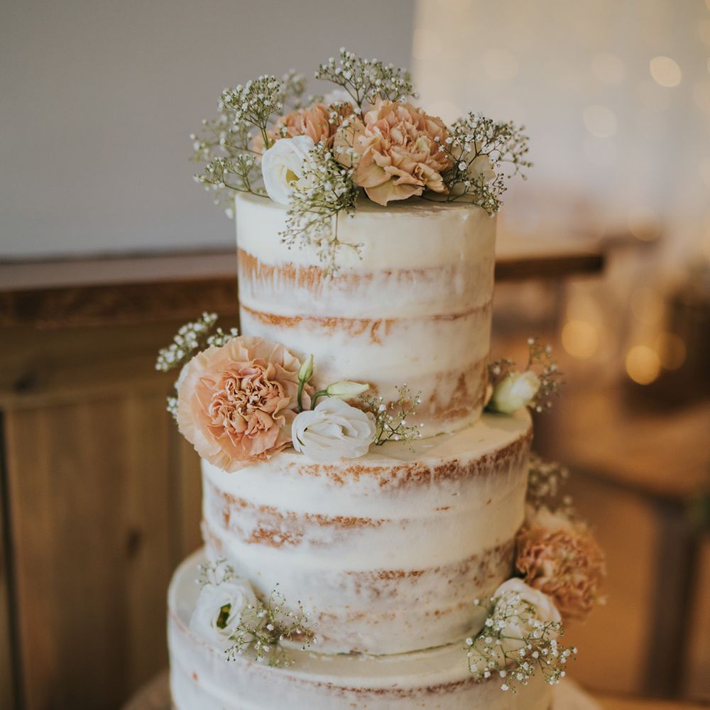 Three tier naked wedding cake with white frosting and floral decor