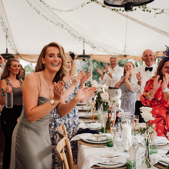 The wedding guests stand and applaud as the bride and groom arrive in for their reception at Pythouse Kitchen Gardens